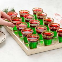 green glasses filled with red liquid sitting on a tray next to candy canes and christmas decorations