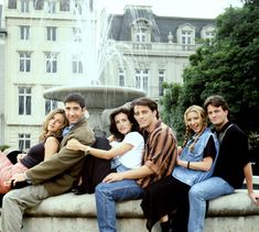 a group of people sitting next to each other near a fountain in front of a building