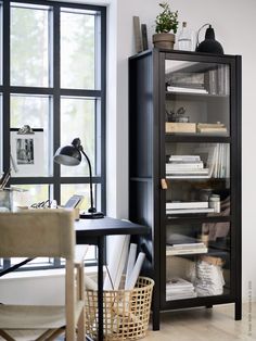 a black bookcase sitting in front of a window next to a desk and chair