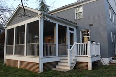 a porch with white railings next to a gray house