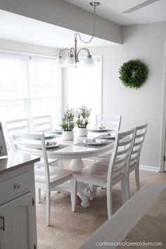 a dining room table with white chairs and a potted plant on the wall behind it