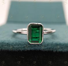 an emerald colored stone is set in a silver ring on top of a blue cloth