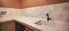 an empty kitchen with white tile walls and brown cupboards on the left side, black faucet in the middle