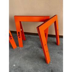 an orange table sitting on top of a cement floor next to a wall with two legs