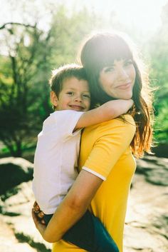 a woman holding a boy in her arms and smiling at the camera with trees in the background