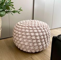 a crocheted poufce sits on the floor next to a potted plant