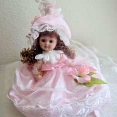 a small doll sitting on top of a pink dress and white bonnet with flowers in it's hair