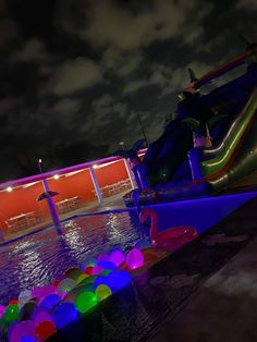 an inflatable water slide is lit up at night with colorful balls on the ground