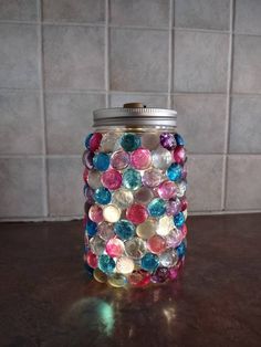 a glass jar filled with lots of different colored buttons on top of a counter next to a tiled wall