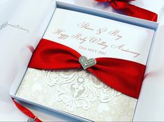 a wedding card with a red bow and diamond brooch on the front in a white box