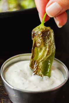 a person dipping some type of food into a small metal bowl filled with white sauce