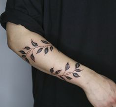 a person with a tattoo on their arm that has leaves on it and is wearing a black t - shirt