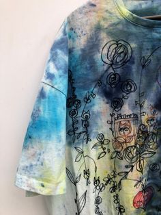 a tie - dyed shirt hanging on a wall with flowers and leaves painted on it