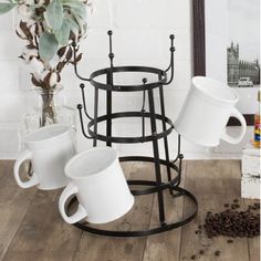 three coffee mugs are stacked on a stand in front of a vase with flowers