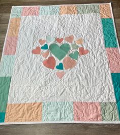 a quilt with hearts on it sitting on a wooden floor next to a piece of cloth