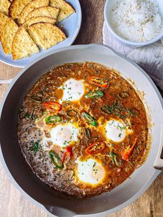 an egg and tomato dish in a bowl on a white tablecloth with utensils