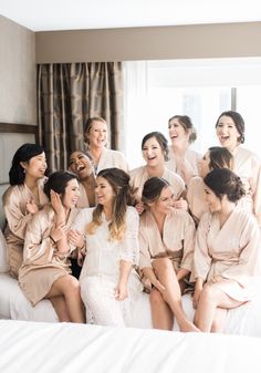 a group of women sitting on top of a bed in matching robes and smiling at the camera