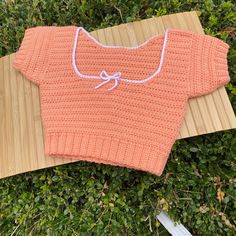 an orange knitted sweater laying on top of a wooden board next to green bushes