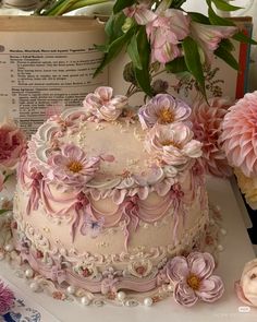 there is a cake with flowers on it and an open book in the back ground