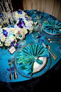 the table is set with blue cloths and silver place settings, along with white flowers