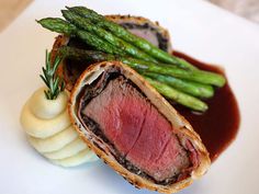 a piece of meat and asparagus on a white plate with red wine sauce