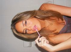 a woman brushing her hair with a pink toothbrush in a bathroom stall while looking at the camera