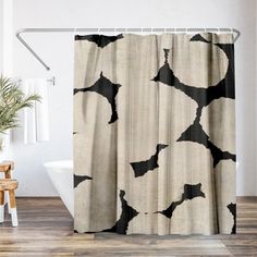 a bathroom with a shower curtain that has black and white designs on it, next to a chair