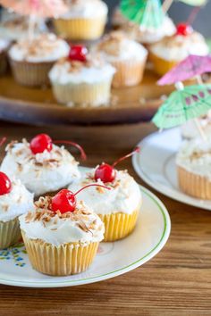 several cupcakes with white frosting and cherries on them are sitting on plates