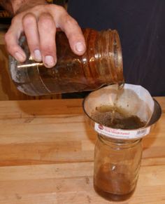 a person pouring something into a glass on top of a wooden table