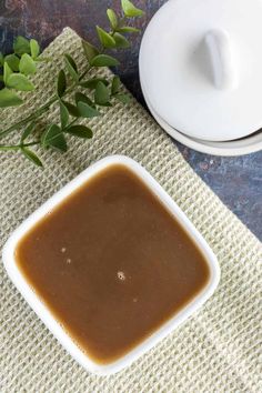 a bowl of brown sauce next to a white plate with green leaves on the side