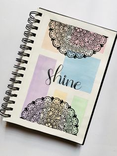 a spiral notebook with the word shine written in black ink on top of colorful papers