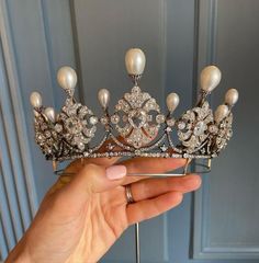 a hand holding a tiara with pearls and diamonds on it's headpiece