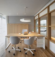 an office with two white chairs and a wooden table in front of large windows on the wall