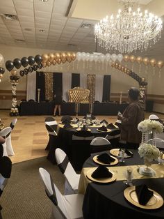 a banquet hall decorated with black and gold tables, white chairs, and large balloons