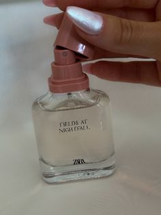 a hand holding a bottle of perfume on top of a white tablecloth with the words spells at nightfau written on it