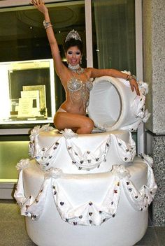 a woman sitting on top of a white cake in front of a glass window with her arms up