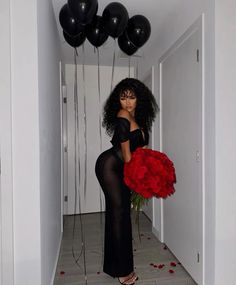 a woman holding a large red flower in a hallway with black balloons and streamers