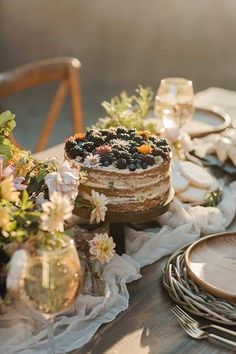 a table topped with a cake covered in blueberries next to plates and glasses filled with wine