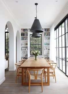 the dining room table is surrounded by chairs and bookshelves with black lamps hanging from them