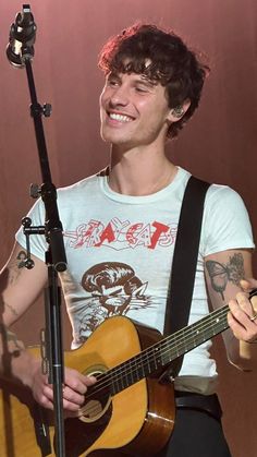 a young man holding a guitar and singing into a microphone