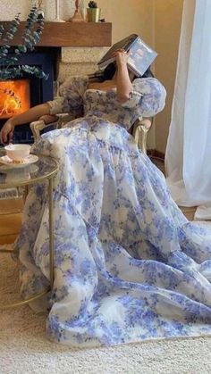 a woman in a blue and white dress sitting on a chair next to a fireplace