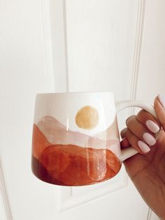 a hand holding a coffee mug with an orange and white design on it, in front of a door