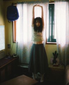 a woman standing in front of a window holding her arms up above her head with both hands