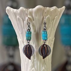 a pair of earrings with beads and leaves on them sitting on a white flower vase