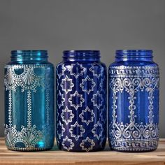 three blue mason jars sitting on top of a wooden table next to each other with designs painted on them