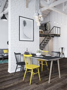 a dining table with yellow chairs in front of a white brick wall and stair case