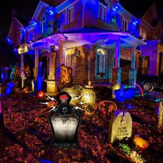 halloween decorations in front of a house with blue and purple lights on the windows, tombstones and headstones