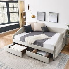 a day bed with drawers underneath it in a living room next to a large window