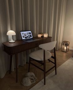 a laptop computer sitting on top of a wooden desk next to a lamp and chair