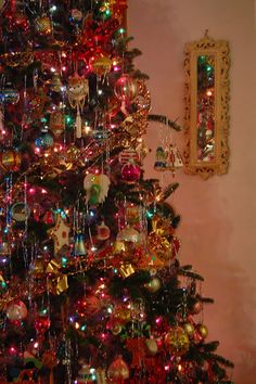 a brightly colored christmas tree with ornaments on it and a mirror in the back ground